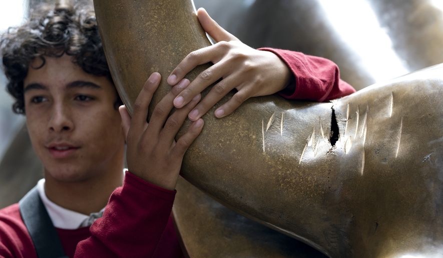 A visitor poses next to the popular lower Manhattan sculpture "Charging Bull," with a damaged right horn, Sunday, Sept. 12, 2019, in New York. A man was arrested Saturday afternoon for damaging the iconic Wall Street Charging Bull statue with an object resembling a banjo, local media reported. (AP Photo/Craig Ruttle)