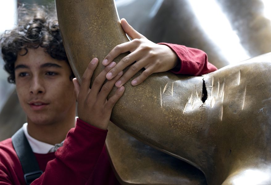 A visitor poses next to the popular lower Manhattan sculpture "Charging Bull," with a damaged right horn, Sunday, Sept. 12, 2019, in New York. A man was arrested Saturday afternoon for damaging the iconic Wall Street Charging Bull statue with an object resembling a banjo, local media reported. (AP Photo/Craig Ruttle)