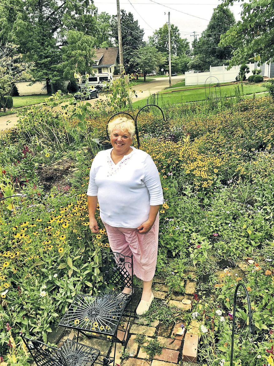 In this Aug. 26, 2019 photo, Mary Beth Durham stands inside the front-yard flower garden at her home in Owensboro, Ky.. She started the flower garden seven years ago, which now stands out among her neighbor's lawns. (Don Wilkins/The Messenger-Inquirer via AP)