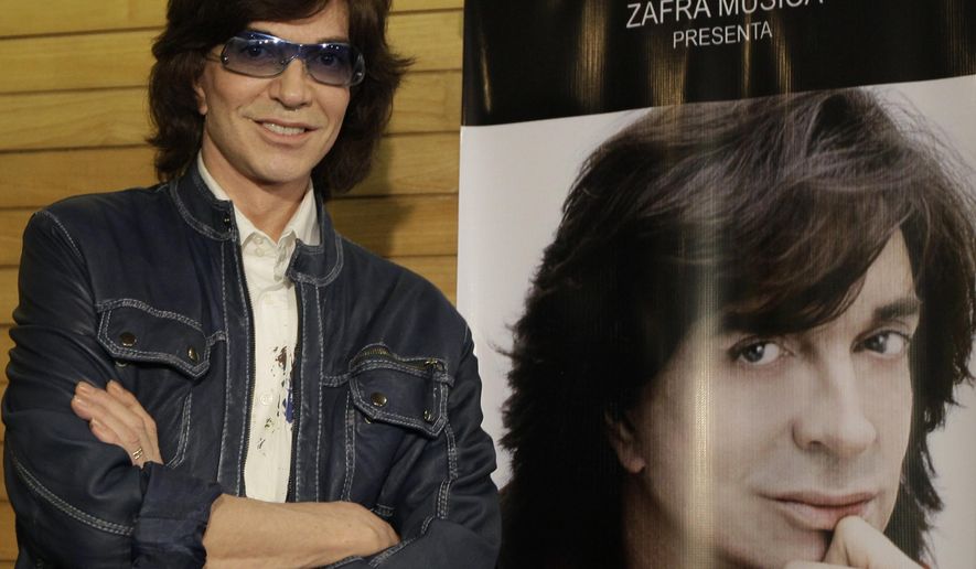 FILE - In this Nov. 4, 2009, file photo, Spanish singer Camilo Sesto poses next to a poster depicting himself during a news conference in Mexico City. Spanish singer and songwriter Camilo Sesto, a popular star in the 1970s and 1980s, has died of heart failure early on Sunday Sept. 8, 2019. He was 72. Sesto, whose real name was Camilo Blanes Cortes, sold more than 100 million records worldwide over his 40-year career. (AP Photo/Gregory Bull, file)