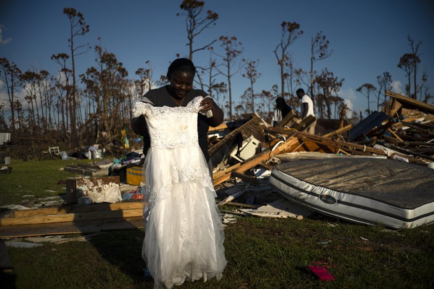 Synobia Reckley holds up the dress her niece wore as a flower girl at her wedding, as she goes through valuables in the rubble of her home destroyed one week ago by Hurricane Dorian in Rocky Creek East End, Grand Bahama, Bahamas, Sunday, Sept. 8, 2019. Synobia, 25, married two days after Hurricane Mathew in 2016, which passed over her home without doing serious damage. (AP Photo/Ramon Espinosa)
