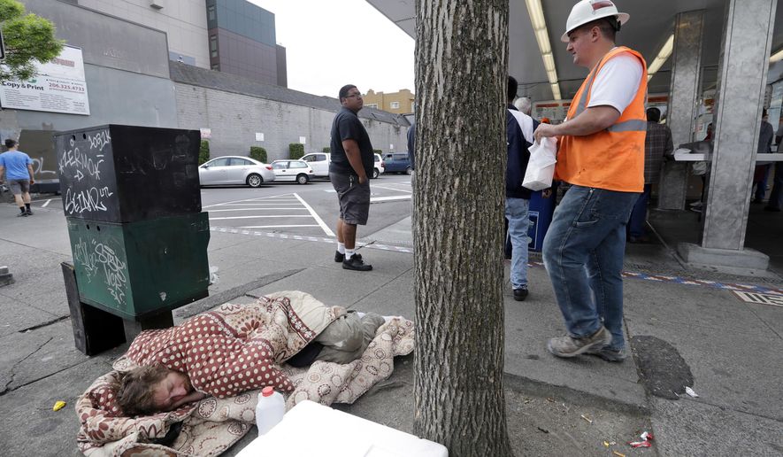 FILE - In this May 24, 2018 file photo, a man sleeps on the sidewalk as people behind line up to buy lunch at a Dick's Drive-In restaurant in Seattle. An elected official in King County, where Seattle is located, wants to dedicate $1 million for one-way bus tickets to relocate homeless people who say they want to reconnect with family outside the region. (AP Photo/Elaine Thompson, File)