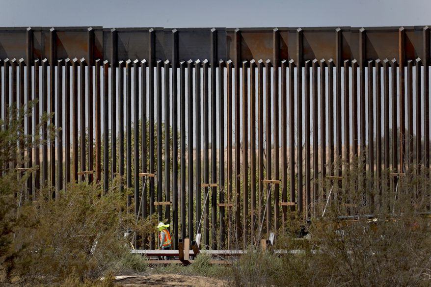 A government contractor walks beside a completed section of Pentagon-funded border wall along the Colorado River, Tuesday, Sept. 10, 2019, in Yuma, Ariz. The 30-foot high wall replaces a five-mile section of Normandy barrier and post-n-beam fencing along the International border that separates Mexico and the United States. Construction began as federal officials revealed a list of Defense Department projects to be cut to pay for President Donald Trump's wall. (AP Photo/Matt York) ** FILE **