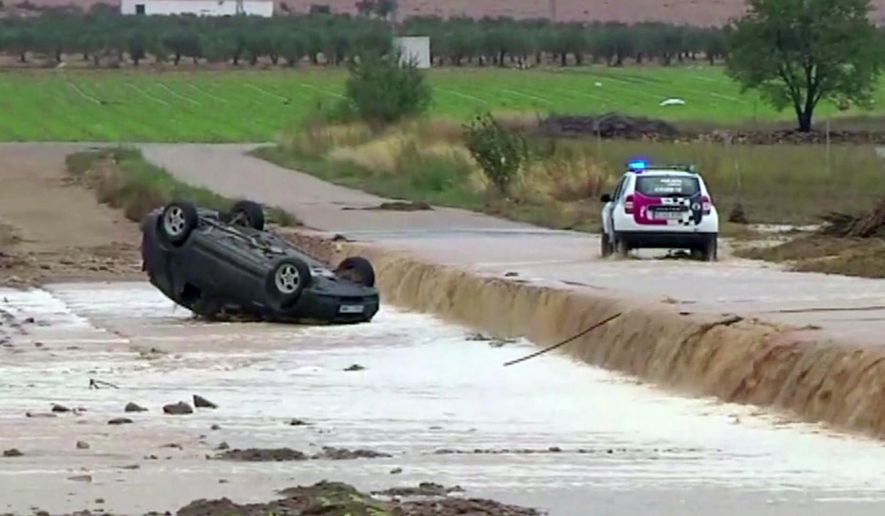 In this image made from video provided by Atlas, a police car drives to an overturned vehicle in which two people were drowned by floodwater, in Caudete, Spain, Thursday, Sept. 12 2019.  A large area of southeast Spain was battered Thursday by what was forecast to be its heaviest rainfall in more than a century, with the storms wreaking widespread destruction and killing at least two people. (Atlas via AP)