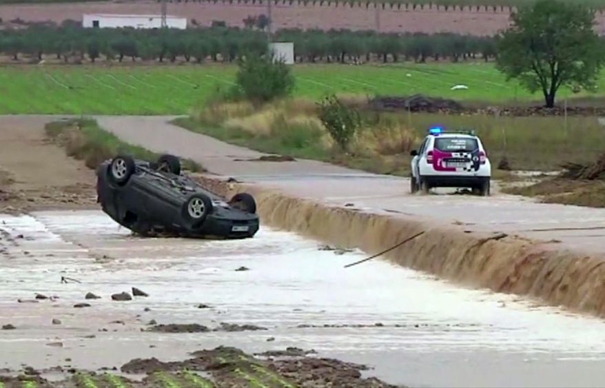 In this image made from video provided by Atlas, a police car drives to an overturned vehicle in which two people were drowned by floodwater, in Caudete, Spain, Thursday, Sept. 12 2019.  A large area of southeast Spain was battered Thursday by what was forecast to be its heaviest rainfall in more than a century, with the storms wreaking widespread destruction and killing at least two people. (Atlas via AP)