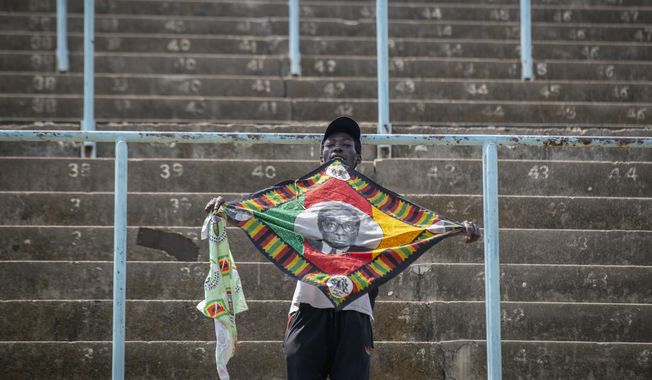 A man in the stands holds a banner with the face of former president Robert Mugabe, as members of the public queue up to view his body at the Rufaro stadium in the capital Harare, Zimbabwe Friday, Sept. 13, 2019. The ongoing uncertainty of the burial of Mugabe, who died last week in Singapore at the age of 95, has eclipsed the elaborate plans for Zimbabweans to pay their respects to the former guerrilla leader at several historic sites. (AP Photo/Ben Curtis)