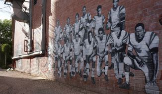 In this Wednesday, Sept. 11, 2019 photo shows part of an alleyway mural in downtown Laramie, Wyo., that honors the Black 14. The Black 14 were black athletes dismissed from the University of Wyoming football team in 1969 for seeking to protest racism by wearing black armbands in a game against Brigham Young University. The university plans to dedicate a plaque honoring the group at War Memorial Stadium on Friday. (AP Photo/Mead Gruver)