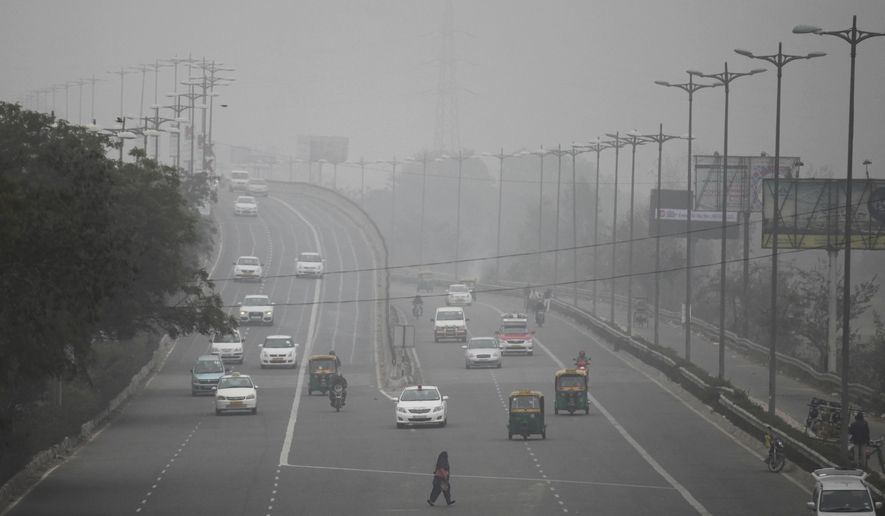 FILE - In this Jan. 15, 2016, file photo, an Indian woman crosses a road as vehicles move through morning smog on the last day of a two-week experiment where the Delhi government allowed private cars on the roads on alternate days depending on whether their license plates end in an even or an odd number, to reduce the number of cars to fight pollution in New Delhi, India. Indian authorities announced an odd-even scheme for movement of private cars in the Indian capital from Nov. 4-15, 2019, after a major Hindu festival that features massive fireworks cloaking the area with toxic smog and dust. (AP Photo/Altaf Qadri, File)