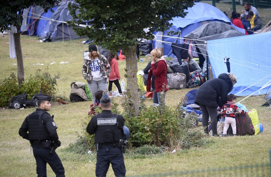 French police officers watch migrants packing their belongings in a camp of Grande Synthe, northern France, Tuesday, Sept.17, 2019. French police are evacuating at least 900 migrants from a gym near the English Channel, citing concerns about security and hygiene. (AP Photo)