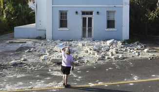 A woman looks up at a building damaged by Hurricane Humberto in Blue Hole Park, Bermuda, Thursday, Sept. 19, 2019. Humberto blew off rooftops, toppled trees and knocked out power but officials said Thursday that the Category 3 storm caused no reported deaths. (AP Photo/Akil J. Simmons) ** FILE **