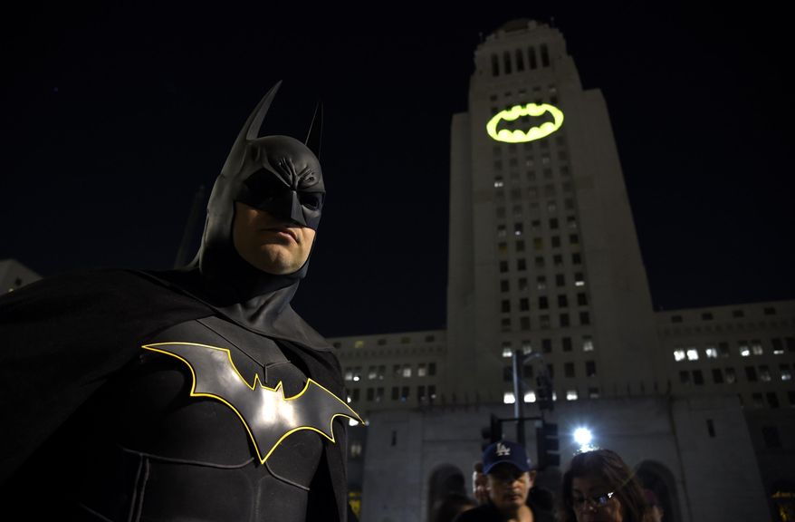 FILE - In this June 15, 2017 file photo, Tony Bradshaw, of Los Angeles, dressed as Batman, poses in front of a Bat-Signal projected onto City Hall during a tribute to "Batman" star Adam West in Los Angeles. The night sky all over the world is lighting up Saturday, Sept. 21, 2019, with an illumination of the famed bat insignia to mark a special anniversary for Batman. DC Comics is carrying off a celebration of "Batman Day" to mark the 80th anniversary of the appearance of crimefighter Bruce Wayne and his masked hidden identity. Fan gatherings are planned all over the world. (Photo by Chris Pizzello/Invision/AP, File)