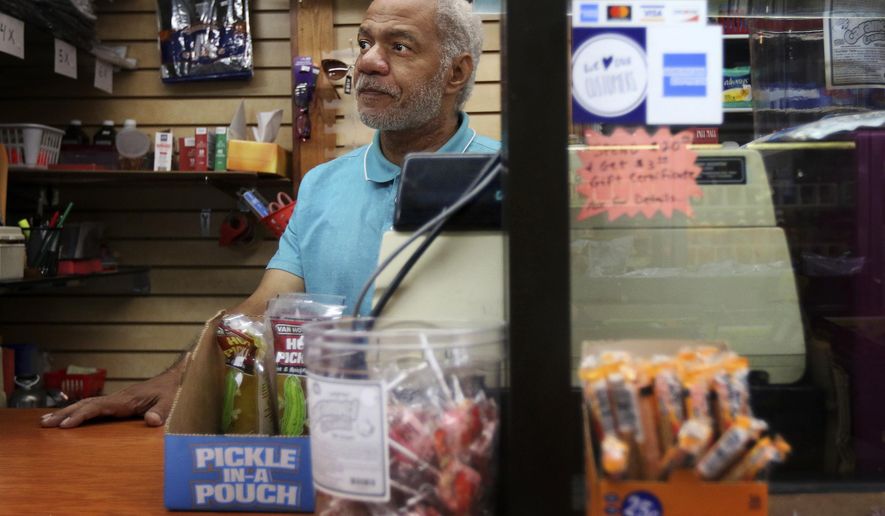 This photo taken Aug. 16, 2019, shows Reginald Stroud, owner of 'Anybody's Dream' convenience store, in Northside, Ohio, standing behind his cash register and a glass barrier while working on Friday. Stroud used to own a home and have a convenience store in the same building on Walnut Street, in downtown Cincinnati, but was displaced when the building was renovated. (Amanda Rossmann/The Cincinnati Enquirer via AP)