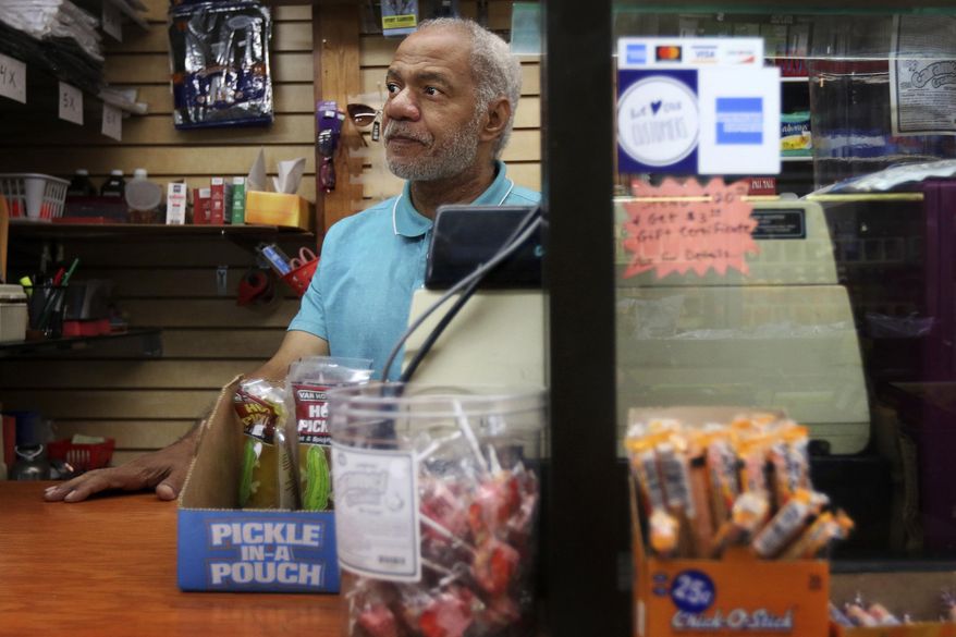 This photo taken Aug. 16, 2019, shows Reginald Stroud, owner of 'Anybody's Dream' convenience store, in Northside, Ohio, standing behind his cash register and a glass barrier while working on Friday. Stroud used to own a home and have a convenience store in the same building on Walnut Street, in downtown Cincinnati, but was displaced when the building was renovated. (Amanda Rossmann/The Cincinnati Enquirer via AP)
