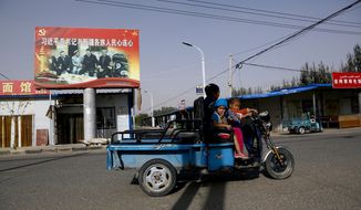 FILE - In this Sept. 20, 2018, file photo, an Uighur woman shuttles school children on an electric scooter as they ride past a propaganda poster showing China&#39;s President Xi Jinping joining hands with a group of Uighur elders in Hotan, in western China&#39;s Xinjiang region. The Trump administration, locked in a trade war with China, is increasing the pressure on Beijing over what it says is the systematic oppression of ethnic minority Muslims. American officials hosted a panel Tuesday, Sept. 24, 2019, on the sidelines of the United Nations General Assembly gathering in New York to highlight the plight of Uighurs, whose native land in China’s far western Xinjiang province they say is a police state. (AP Photo/Andy Wong, File)
