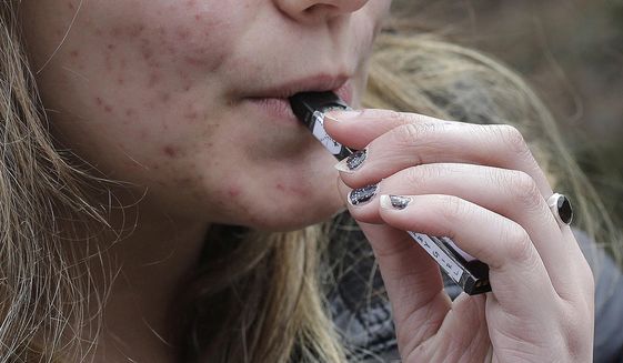 In this April 11, 2018, file photo, a high school student uses a vaping device near a school campus in Cambridge, Mass. (AP Photo/Steven Senne, File)
