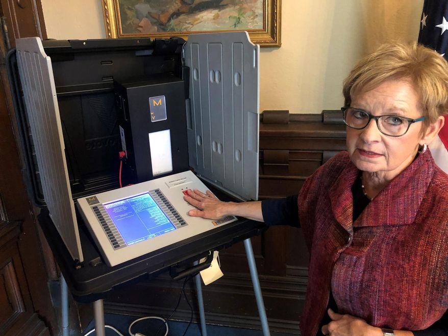 In this Sept. 25, 2019 photo, Indiana Secretary of State Connie Lawson demonstrates an upgraded voting machine on Wednesday, Sept. 25, 2019, at the Indiana Statehouse office in Indianapolis. The state is buying the boxes at the rear right of the voting booth that will display a paper printout allowing voters to double-check how their vote is recorded on the electronic machines. (AP Photo/Tom Davies)