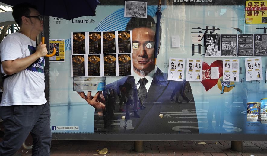 In this Sept. 15, 2019, photo, a man holding an umbrella walks by a bus stop advertisement filled with protest art posters. As Hong Kong enters its fourth month of steady protests, the city is embracing for another violent weekend prior to the upcoming 70th National Day on Oct. 1. (AP Photo/ Vincent Yu)
