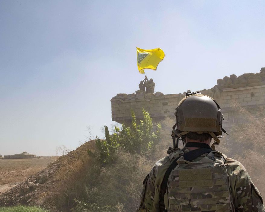 In this Sept. 21, 2019, photo, released by the U.S. Army, a U.S. soldier oversees members of the Syrian Democratic Forces as they demolish a Kurdish fighters&#39; fortification and raise a Tal Abyad Military Council flag over the outpost as part of the so-called &amp;quot;safe zone&amp;quot; near the Turkish border. (U.S. Army photo by Staff Sgt. Andrew Goedl via AP)