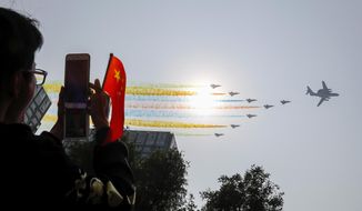 A man uses his smartphone to film Chinese military planes trail colored smoke as they fly in formation past the sun during a parade to commemorate the 70th anniversary of the founding of Communist China in Beijing, Tuesday, Oct. 1, 2019. China&#39;s Communist Party is celebrating its 70th anniversary in power with a parade showcasing its economic development and newest weapons. The event marks the anniversary of the Oct. 1, 1949, announcement of the founding of the People&#39;s Republic of China by then-leader Mao Zedong. (AP Photo/Andy Wong)