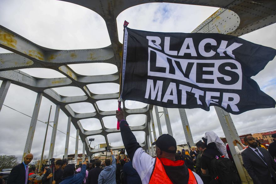 In this March 3, 2019, file photo, Black Lives Matter demonstrator waves a flag on the Edmund Pettus Bridge during the Bloody Sunday commemoration in Selma, Ala. On Nov. 13, the AP reported that a local school board in Burlington, Vt., gave its permission to an area middle school to fly the banner on campus. (AP Photo/Julie Bennett, File)