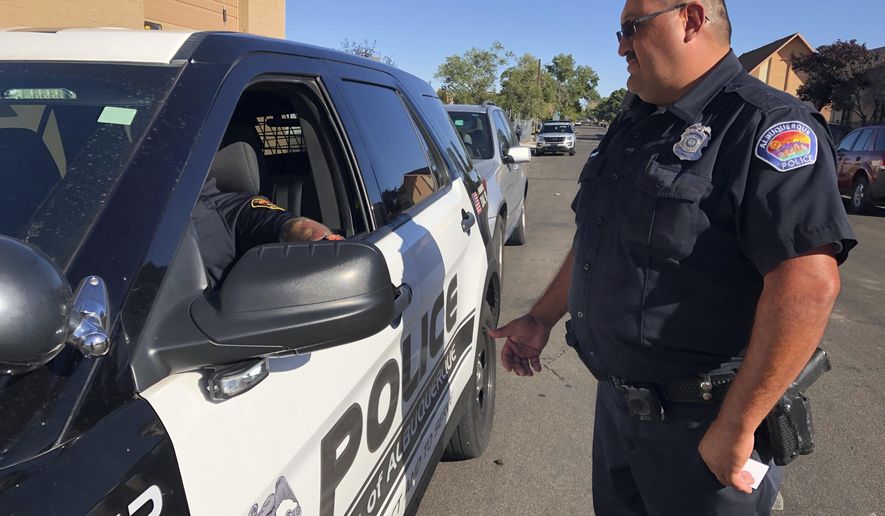 Officer Dennis Torres stands next to a patrol vehicle as he talks with his sergeant on Wednesday, Oct. 2, 2019, in Albuquerque, New Mexico. FBI figures show both Albuquerque and New Mexico had significantly higher violent crime rates than the nationwide rate of 368.9 offenses per 100,000 residents in 2018. (AP Photo/Mary Hudetz)