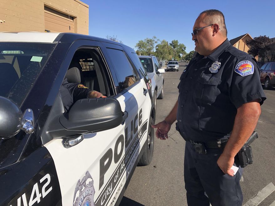 Officer Dennis Torres stands next to a patrol vehicle as he talks with his sergeant on Wednesday, Oct. 2, 2019, in Albuquerque, New Mexico. FBI figures show both Albuquerque and New Mexico had significantly higher violent crime rates than the nationwide rate of 368.9 offenses per 100,000 residents in 2018. (AP Photo/Mary Hudetz)