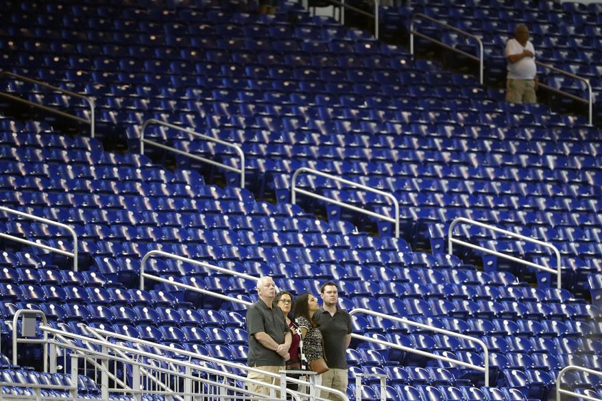 FILE - In this Monday, Sept. 9, 2019 file photo,Baseball fans stand among empty seats during the singing of the national anthem before a baseball game between the Miami Marlins and the Milwaukee Brewers in Miami. Major League Baseball's average attendance dropped 1.7% this year for its fourth straight decline, and five of the six biggest drops were by teams with losing records. The 30 teams averaged 28,339, according to the commissioner's office, down from 28,830 last year _ the first time the average was below 30,000 since 2003. (AP Photo/Wilfredo Lee, File)