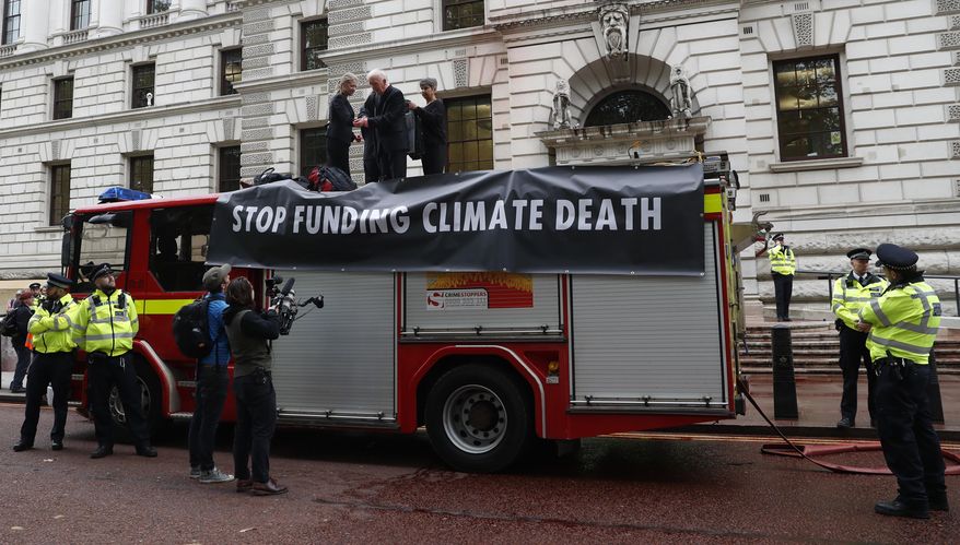 Extinction Rebellion climate activists stand on a fire engine outside the Treasury building in London, Thursday, Oct. 3, 2019. Climate activists sprayed hundreds of liters (gallons) of fake blood on the British government building, hoping to underscore the damage humans are causing to the planet. (AP Photo/Alastair Grant)