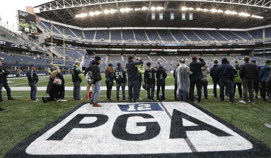 Fans stand near a logo on the turf at CenturyLink Field honoring former Seattle Seahawks owner Paul G. Allen, who died in 2018, before an NFL football game between the Seahawks and the Los Angeles Rams, Thursday, Oct. 3, 2019, in Seattle. The Seahawks were scheduled to induct Allen into the team's Ring of Honor during a pregame ceremony. (AP Photo/Elaine Thompson)