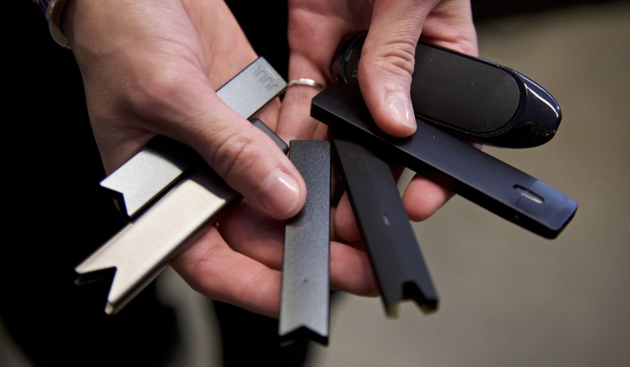 FILE - In this April 16, 2019, file photo, a researcher holds vape pens in a lab at Portland State University in in Portland, Ore. As of October 2019, experts who examined lung tissue from 17 patients say lung damage reported in people who use e-cigarettes and other vaping devices looks like chemical burns similar to what you’d see in people exposed to poisonous gases. (AP Photo/Craig Mitchelldyer, File)