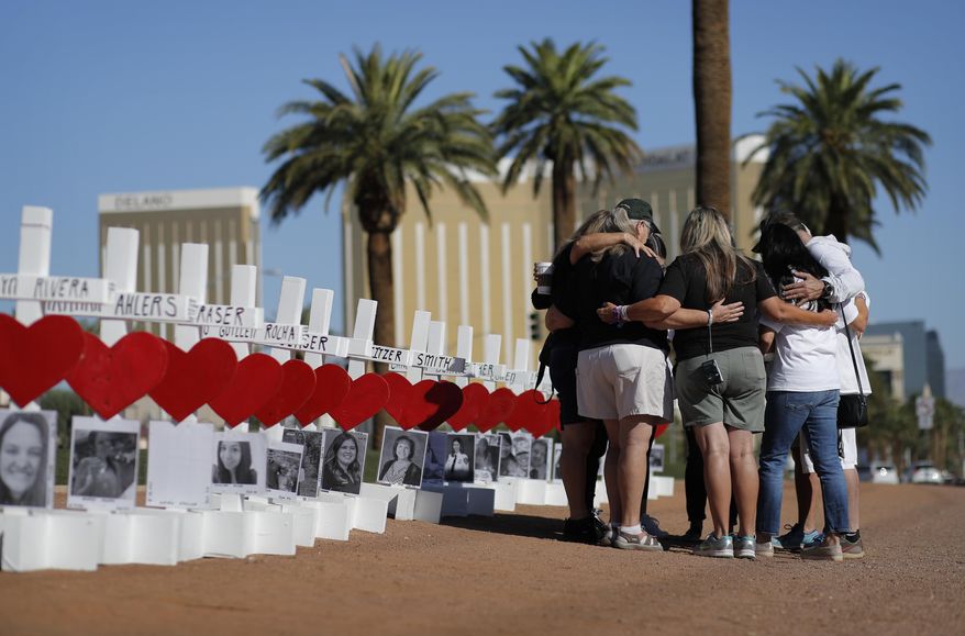 In this Oct. 1, 2019, file photo, people pray at a makeshift memorial for shooting victims in Las Vegas, on the anniversary of the mass shooting two years earlier. Two years after a shooter rained gunfire on country music fans from a high-rise Las Vegas hotel, MGM Resorts International reached a settlement that could pay up to $800 million to families of the 58 people who died and hundreds of others who were injured, attorneys announced Thursday, Oct. 3, 2019. (AP Photo/John Locher, File)