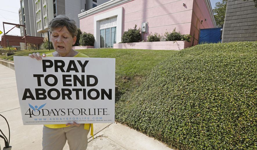 FILE - In this Oct. 2, 2019 file photo, an abortion opponent sings to herself outside the Jackson Womens Health Organization clinic in Jackson, Miss. Three judges from a conservative federal appeals court are hearing arguments, Monday, Oct. 7, over a Mississippi law that would ban most abortions after 15 weeks of pregnancy. Republican Gov. Phil Bryant signed the law in 2018, the state’s only abortion clinic immediately sued and U.S. District Judge Carlton Reeves blocked the law from taking effect. (AP Photo/Rogelio V. Solis)