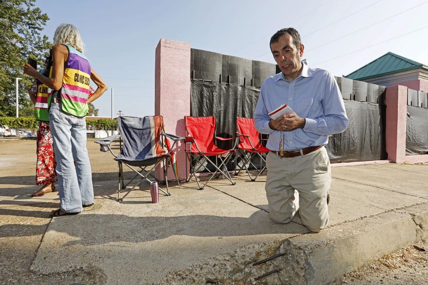 Dani Choufani recites the rosary outside the Jackson Women's Health Organization clinic, while clinic escorts wait for incoming patients in Jackson, Miss., Wednesday, Oct. 2, 2019. The Jackson City Council voted 3-1 Tuesday to enact a local law limiting amplified sound outside health care facilities and creating buffer zones to move protesters further from the entrances. The law is set to take effect in about a month, and opponents say it unconstitutionally limits their right to free speech. A court challenge is likely. (AP Photo/Rogelio V. Solis)