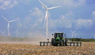FILE - In this Aug. 17, 2015, file photo, a farmer plows his recently harvested field under wind turbines in the agricultural area north of Rio Hondo, Texas, near the New Mexico border. A California-based renewable energy developer plans to increase by seven-fold its investments as it prepares to build more wind farms in the heart of New Mexico over the next several years. An analysis commissioned by Pattern Development shows a $1.2 billion economic impact from its wind farms in eastern New Mexico and West Texas, surpassing initial projections. (Jason Hoekema/Valley Morning Star via AP, File)