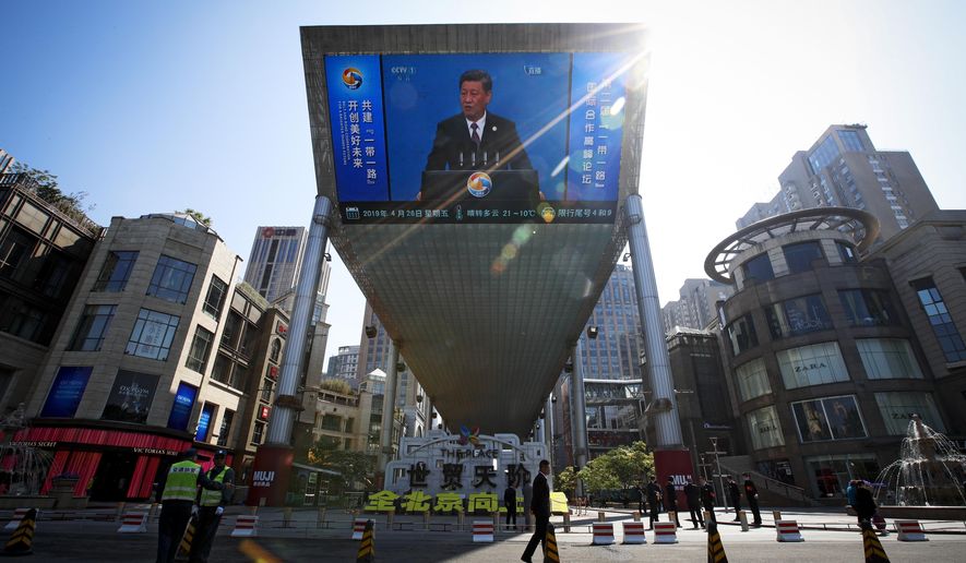 FILE - In this April 26, 2019, file photo, traffic warden and securities stand guard near a TV screen broadcasting live of President Xi Jinping's opening speech, outside a shopping mall in Beijing. Companies who do business with China walk a fine line to stay aligned with U.S. values such as freedom of speech and democracy while avoiding offending China, where they stand to make billions of dollars. (AP Photo/Andy Wong, File)