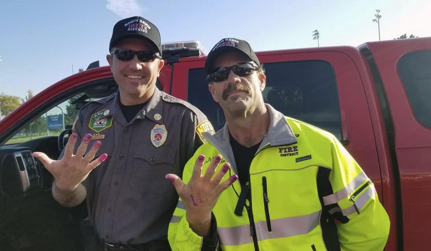 This Friday, Oct. 11, 2019, photo released by the North Davis Fire District shows Chief Allen Hadley, left, and Cpt. Kevin Lloyd In Clearfield, Utah. The two Utah firefighters are receiving praise after they found a creative way to keep a young girl calm at the scene of a car accident. North Davis Fire District Fire Chief Mark Becraft said the firefighters let a young girl paint their nails after she and her mother were in a car accident Saturday. Chief Hadley and Cpt. Lloyd checked on the crying and screaming girl while medics evaluated her mother. Nobody was seriously injured. (Charlotte Coyle/North Davis Fire District via AP)
