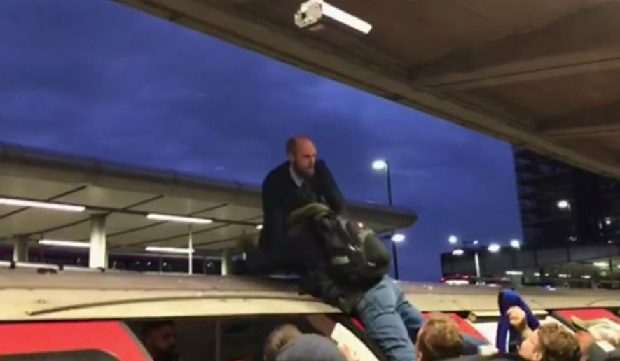 In this image taken from video, a man grabs a protester on top of a train, in London, Thursday Oct. 17, 2019. Angry commuters scuffled with climate activists who climbed onto the roofs of trains, snarling services in the busy morning rush hours in the British capital. (ITN via AP)