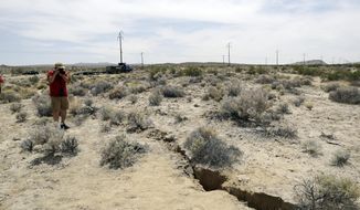 FILE - In this July 7, 2019 file photo, a visitor takes a photo of a crack in the ground following recent earthquakes near Ridgecrest, Calif. Scientists say the earthquakes that hammered the Southern California desert near the town of Ridgecrest last summer involved ruptures on a web of interconnected faults and increased strain on a major nearby fault that has begun to slowly move. (AP Photo/Marcio Jose Sanchez, File)