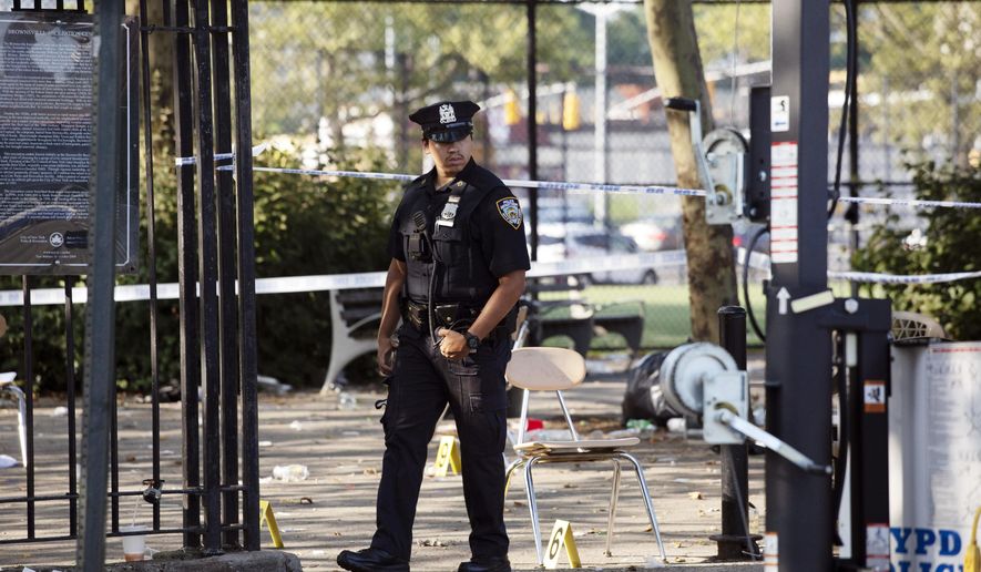 FILE - In this July 28, 2019 file photo, a police officer walks by yellow evidence markers at a playground after a shooting in the Brownsville neighborhood in the Brooklyn borough of New York. New York City police have made an arrest in the community festival shooting that left one person dead and 11 wounded this summer. Police said Wednesday, Oct. 16, that 20-year-old Kyle Williams, of Brooklyn, was arrested on murder, criminal possession of a weapon, reckless endangerment and attempted murder charges. (AP Photo/Mark Lennihan, File)
