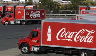 In this Monday, Oct. 14, 2019 photo a truck with the Coca-Cola logo, behind left, maneuvers in a parking lot at a bottling plant in Needham, Mass. The Coca-Cola Co. reports financial results Friday, Oct. 18. (AP Photo/Steven Senne)