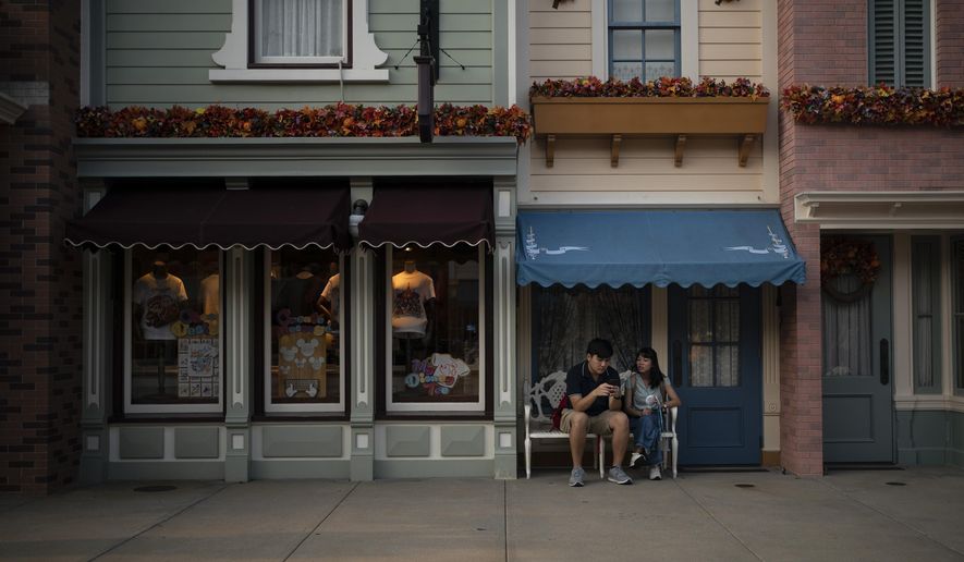 In this Oct. 11, 2019 photo, visitors sits outside a shop on the Main Street at Hong Kong Disneyland in Hong Kong. The body-blow of months of political protests on Hong Kong’s tourism is verging on catastrophic for one of the world’s great destinations. Geared up to receive 65 million travelers a year, the city’s hotels, retailers, restaurants and other travel-oriented industries are suffering. But some intrepid visitors came specifically to see the protests and are reveling in deep discounts and unusually short lines at tourist hotspots. (AP Photo/Felipe Dana)