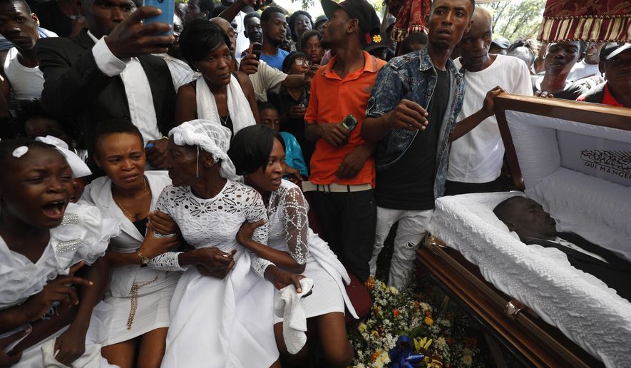 Family members grieve beside the coffin of one of the men killed during a month of demonstrations aimed at ousting Haitian President Jovenel Moïse, during a joint funeral for two victims in a public plaza near the National Palace in central Port-au-Prince, Haiti, Wednesday, Oct. 16, 2019. (AP Photo/Rebecca Blackwell)