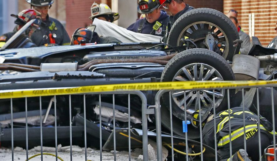 Indianapolis Fire Department personnel work the scene where a vehicle plummeted from an upper level of a parking garage in Indianapolis, Wednesday, Oct. 23, 2019, landing inverted in the alley behind the City Market. Two fatalities were found in the vehicle. The incident is now under a death investigation. (Kelly Wilkinson, Indianapolis Star via AP)