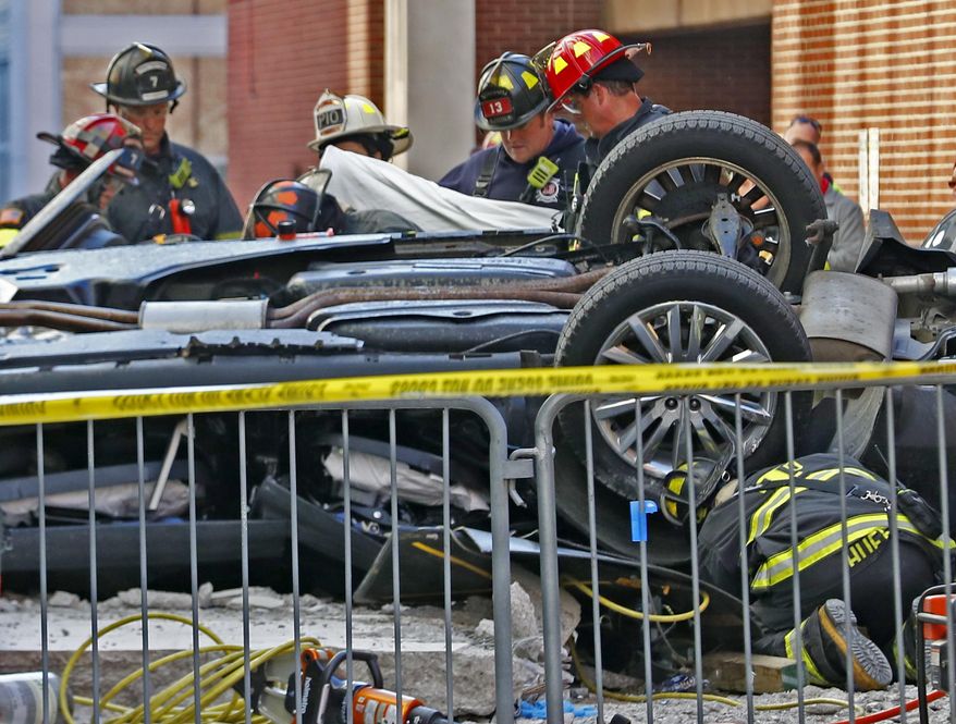 Indianapolis Fire Department personnel work the scene where a vehicle plummeted from an upper level of a parking garage in Indianapolis, Wednesday, Oct. 23, 2019, landing inverted in the alley behind the City Market. Two fatalities were found in the vehicle. The incident is now under a death investigation. (Kelly Wilkinson, Indianapolis Star via AP)