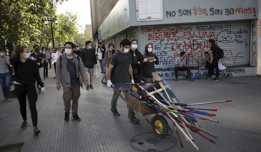 Students push a wheelbarrow as they work to clean the streets damaged by anti-government protests in Santiago, Chile, Thursday, Oct. 24, 2019. Chile has been facing days of unrest, triggered by a relatively minor increase in subway fares. The protests have shaken a nation noted for economic stability over the past decades, which has seen steadily declining poverty despite persistent high rates of inequality. (AP Photo/Rodrigo Abd)