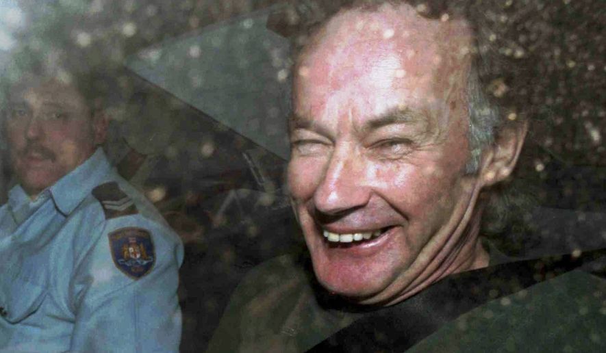 FILE - In this Nov. 4, 1997, file photo, Ivan Milat smiles in a police car after attending a court in Sydney, Australia. Milat, whose grisly serial killings of young backpackers horrified Australians in the early '90s, died in a Sydney prison on Sunday, Oct. 27, 2019, prison authorities said. He was 74. (AP Photo/Rick Rycroft, File)