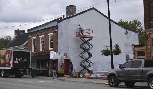 From the top of the lift, Anna Murphy puts white primer on the side of Bourbon on Main in Frankfort, Ky., Oct. 16, 2019, while her parents, Paula and Shaun Murphy, use painters&#x27; tape to protect a few corners of the mural. (McKenna Horlsey/The State Journal via AP)