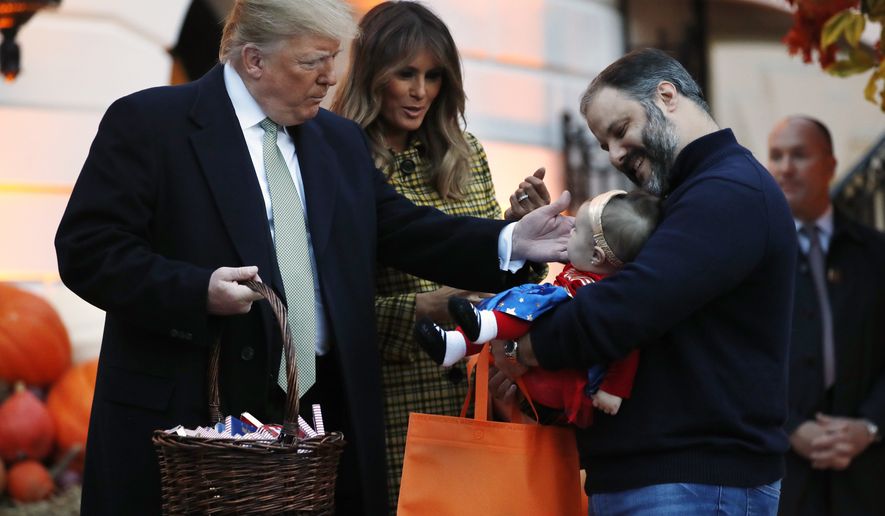 President Donald Trump and first lady Melania Trump greet a baby in a superhero costume as they hand out candy to children during a Halloween trick-or-treat event at the White House, Sunday, Oct. 28, 2018, in Washington. (AP Photo/Jacquelyn Martin)