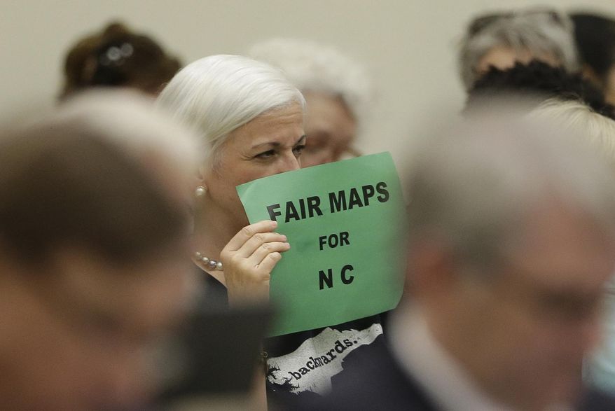 In this July 26, 2017 photo, a member of the gallery tries to display her sign while lawmakers convene during a joint select committee meeting on redistricting in Raleigh, N.C. North Carolina judges on Monday blocked the state's congressional map from being used in the 2020 elections, ruling that voters had a strong likelihood of winning a lawsuit that argued Republicans unlawfully manipulated district lines for partisan gain. (AP Photo/Gerry Broome)
