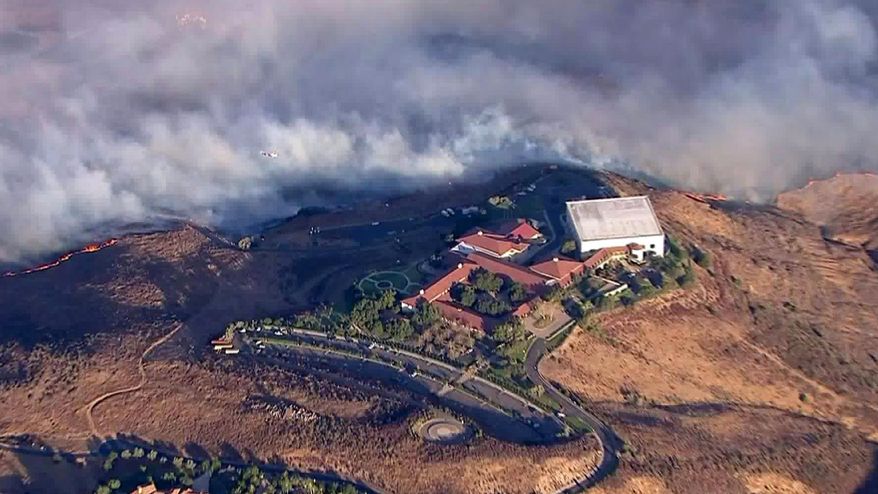 This photo from video provided by KTLA-TV shows the Ronald Reagan Presidential Library as flames from the Easy fire approach in Simi Valley, Calif., Wednesday, Oct. 30, 2019. The new wildfire erupted in wind-whipped Southern California, forcing the evacuation of the Library and nearby homes, as both ends of the state struggled with blazes, dangerously gusty weather and deliberate blackouts. Library spokeswoman Melissa Giller said the hilltop museum was safe (KTLA-TV via AP)